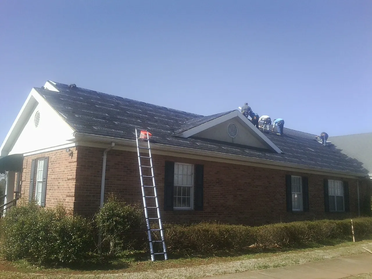 Crew tearing shingles off a brick ranch roof with a ladder set — Metal Roof Repair work by our crew in Canadensis