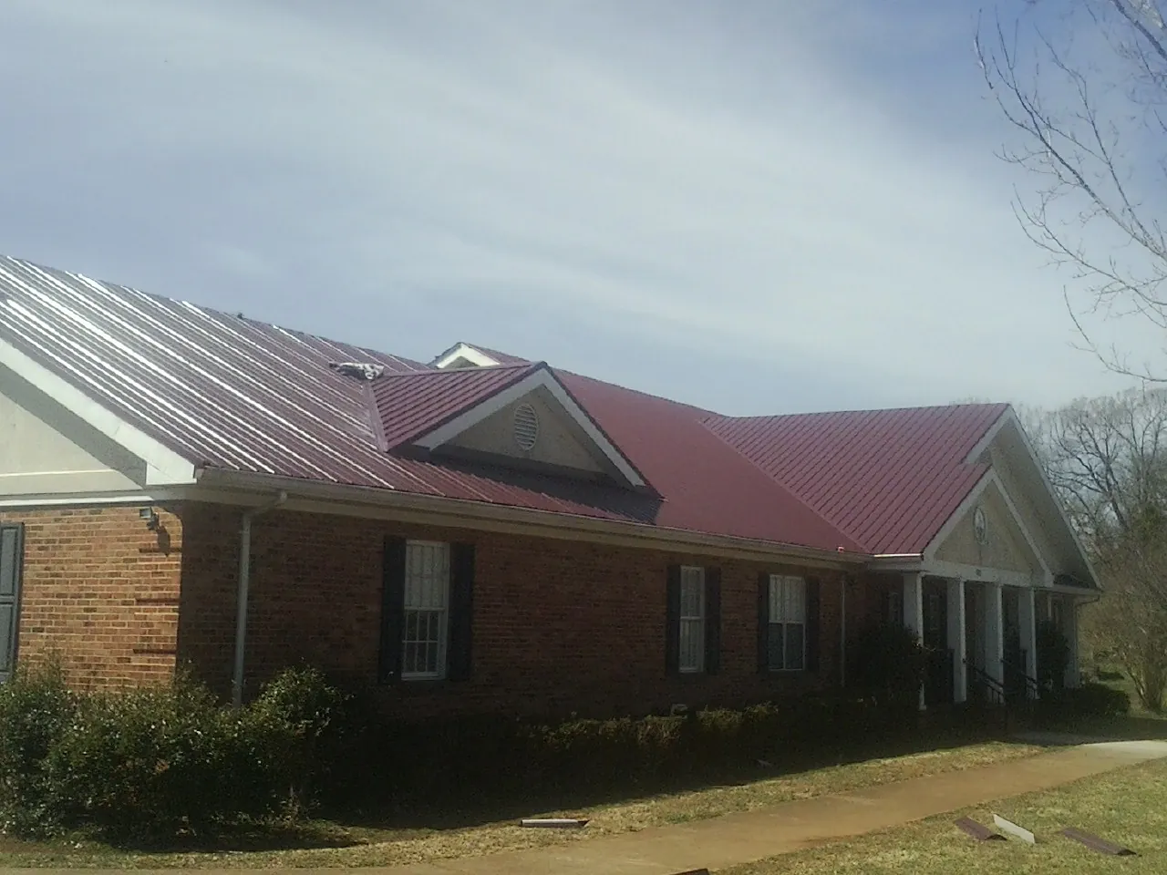 Red metal roof with gabled entries on a long brick building, from a Hail Damage Roof Repair job in Canadensis