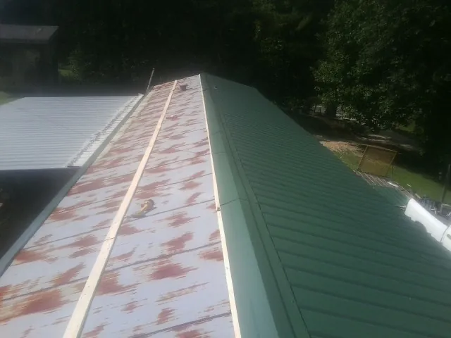Old rusted panels beside newly installed green metal roofing — Wind Damage Roof Repair by Roofing Brothers in Canadensis