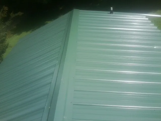 New green metal panels meeting at the ridge of a roof — Flat Roof Repair work by our crew in Canadensis