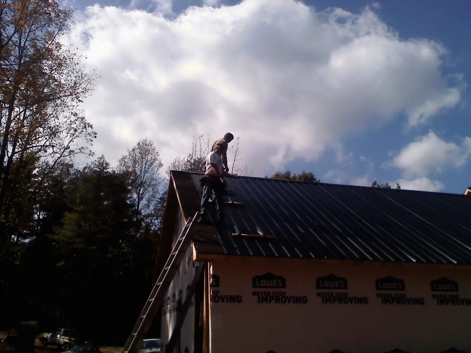 Roofer fastening dark metal panels high against a cloudy sky, from a Roof Inspection job in Canadensis