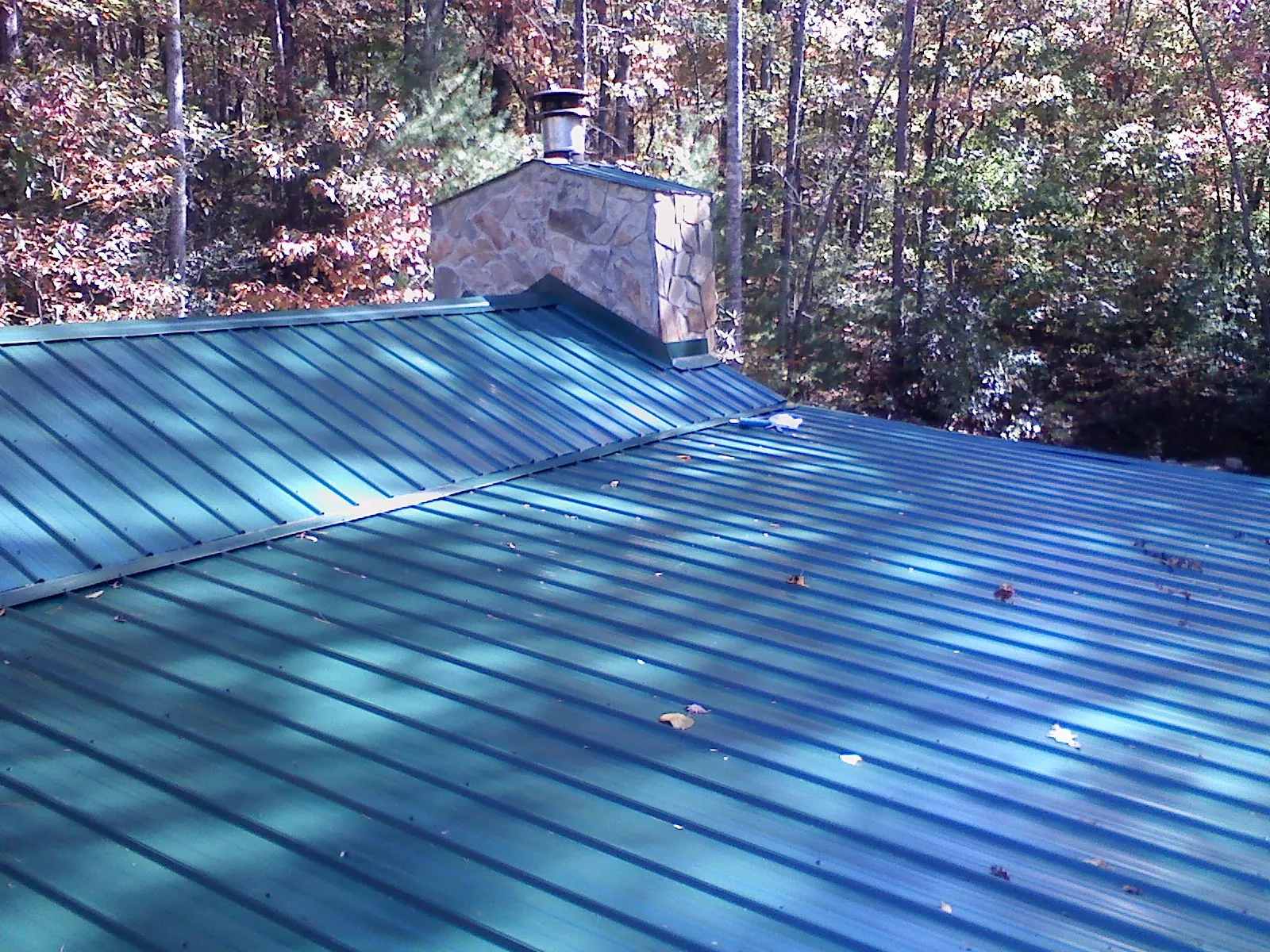 New green metal roof and stone chimney surrounded by autumn woods in Canadensis