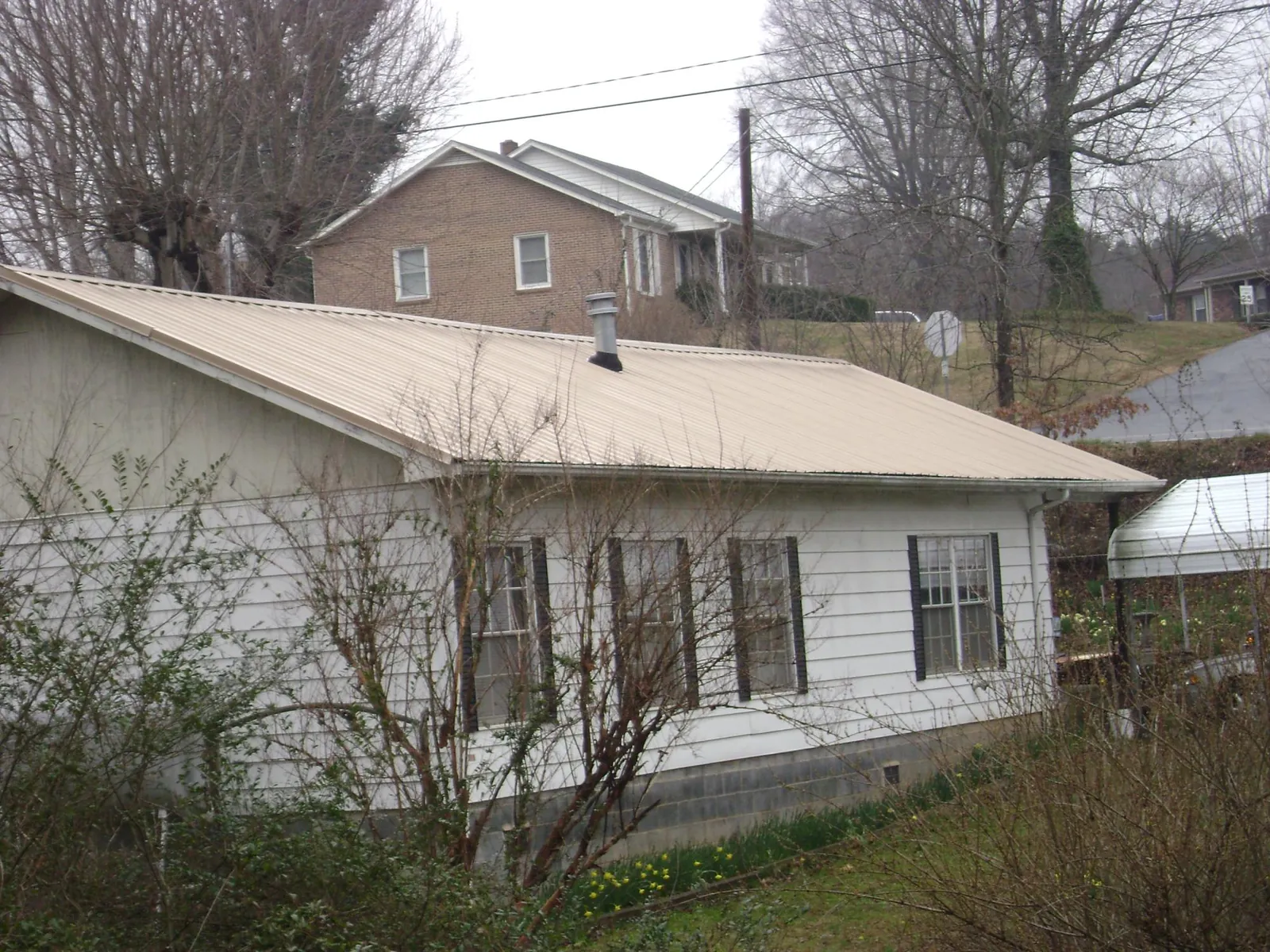 Tan metal roof on a white sided house set into a hillside — Commercial Roofing by Roofing Brothers in Canadensis